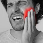 Man experiencing severe toothache, holding his face in pain, emphasizing the urgency of dental emergencies.