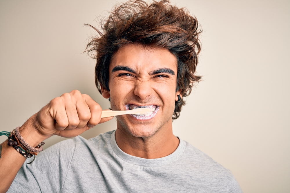 Young man brushing teeth with wooden toothbrush and toothpaste, emphasizing oral hygiene and daily dental care.
