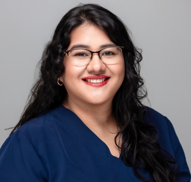 Carolina, dental assistant at Robles Family Dental, smiling in a blue scrubs top against a neutral background.