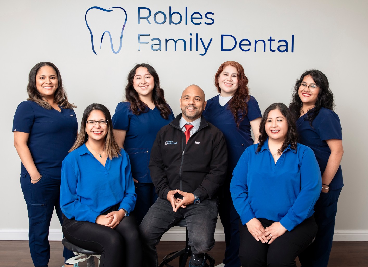 Robles Family Dental team, featuring Dr. Kenny Robles, providing emergency dental care in Berwyn, with staff in blue scrubs and a dental logo backdrop.