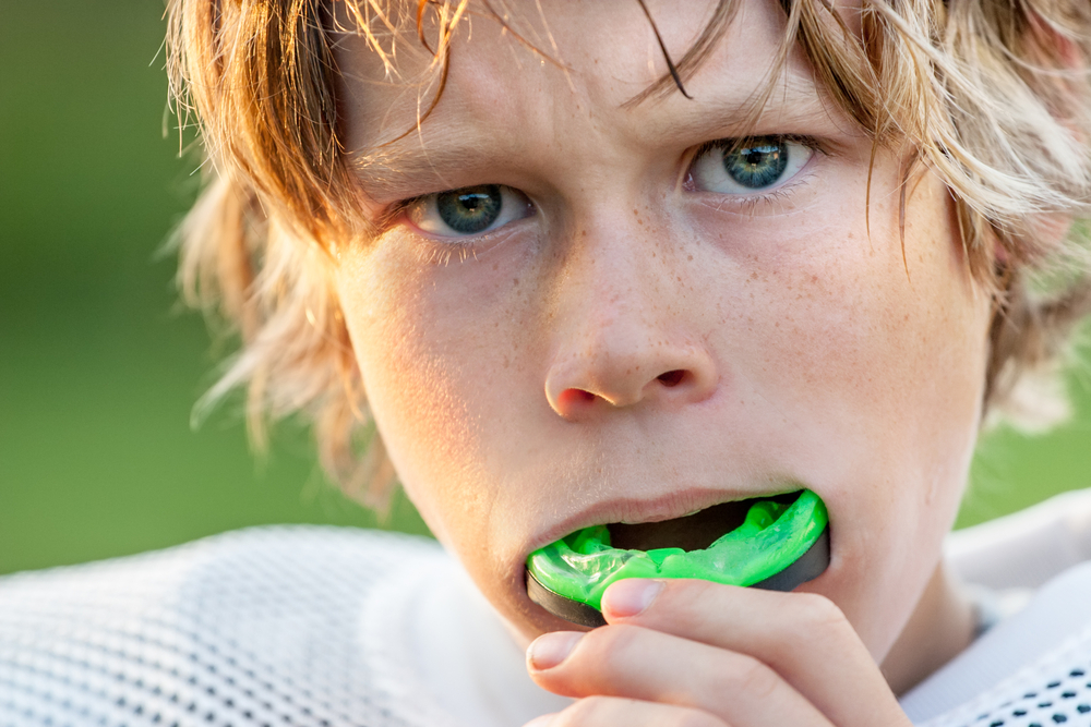 Boy wearing a green mouthguard, preparing for contact sports, emphasizing dental safety and prevention of tooth avulsion.