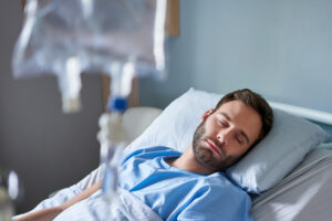 Man resting in a hospital bed with an IV drip, illustrating the effects of IV sedation during dental procedures for managing anxiety.