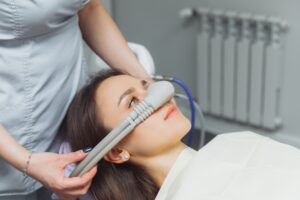 Woman receiving nitrous oxide sedation during dental procedure, with a dental professional administering the gas through a mask, promoting relaxation and anxiety relief.