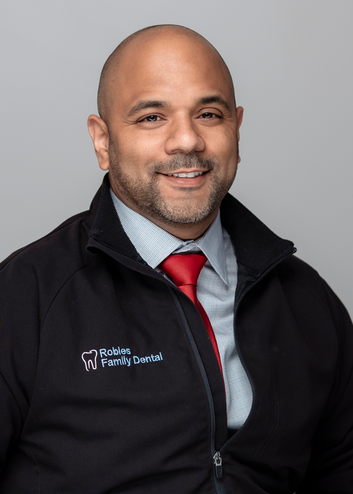 Dr. Kenny Robles wearing a black jacket with "Robles Family Dental" logo, smiling, representing emergency dental care for cracked or broken teeth in Berwyn, IL.
