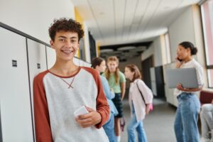 Teen boy smiling confidently in school hallway, showcasing improved self-esteem and social interaction, reflecting positive effects of orthodontic treatment like Invisalign Teen.