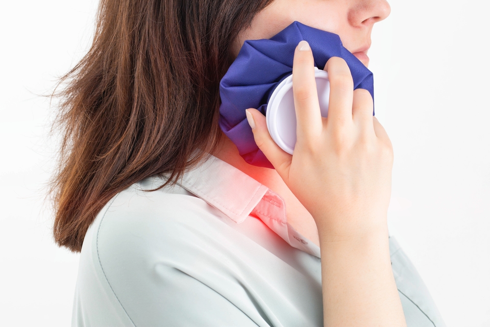 Woman applying ice pack to cheek for dental pain relief, illustrating emergency dental care at Robles Family Dental.