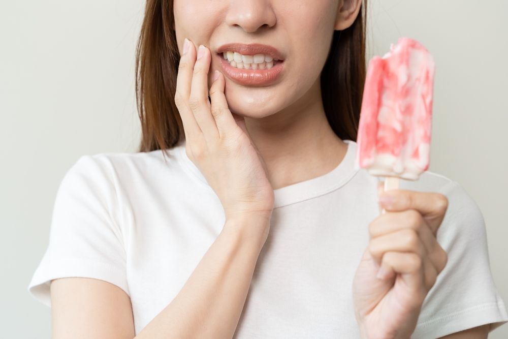 Woman holding a popsicle while experiencing tooth sensitivity, indicating potential dental issues related to cracked or broken teeth.