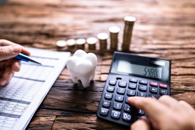 Person calculating dental expenses with a calculator and dental model, alongside a financial chart and coins, illustrating budgeting for dental insurance options.
